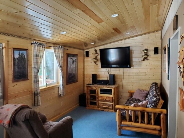 A wooden cabin interior with a TV mounted on the wall, a wooden bench, and a couch.