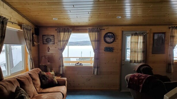Ein gemütliches Cabin-Interieur mit Holzbalkendecke, einem braunen Ledersofa, einem kleinen Tisch und einem Fenster mit Vorhängen.