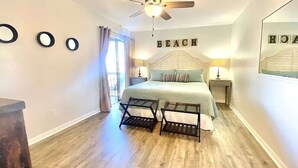 A bedroom with a bed, two nightstands, a ceiling fan, and a wall with the word "BEACH" above the bed. - Clean & Ready for Guests! Recently Remodeled, Steps to the Beach! (Miramar Beach)