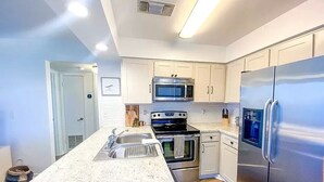 A modern kitchen with white cabinets, stainless steel appliances, and a granite countertop. - Clean & Ready for Guests! Recently Remodeled, Steps to the Beach! (Miramar Beach)