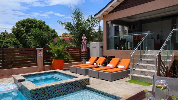 Uma área de piscina com duas banheiras de hidromassagem, espreguiçadeiras e uma escadaria que leva a um andar superior.