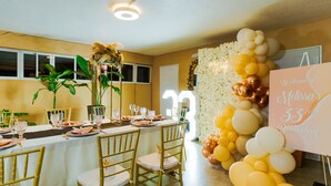 Um espaço interno bem iluminado com uma mesa comprida posta para refeição, rodeada por cadeiras.
