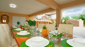 Uma sala de jantar com uma mesa comprida posta para refeição, um espelho na parede e vista para o exterior.