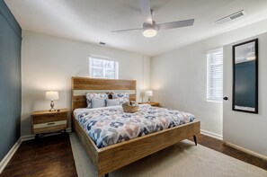 Una camera da letto con un letto di legno, due comodini con lampade, una ventola a soffitto e una grande finestra.