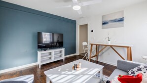 A modern living room with a flat-screen TV on a white stand, a ceiling fan, and a dining area with a small table and chairs. - 5min-Grant park|Fenced Yard|Parking|Fire Pit&BBQ (Atlanta)
