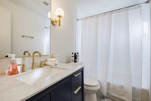 Un bagno con un lavandino bianco, rubinetti dorati, uno specchio grande e una tenda da doccia.