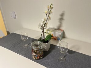 Un piccolo tavolo con un vaso di orchidee bianche, un barattolo di cioccolatini e due bicchieri vuoti.