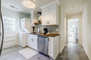 A modern kitchen with white cabinetry, a stainless steel dishwasher, and a herringbone-patterned backsplash.