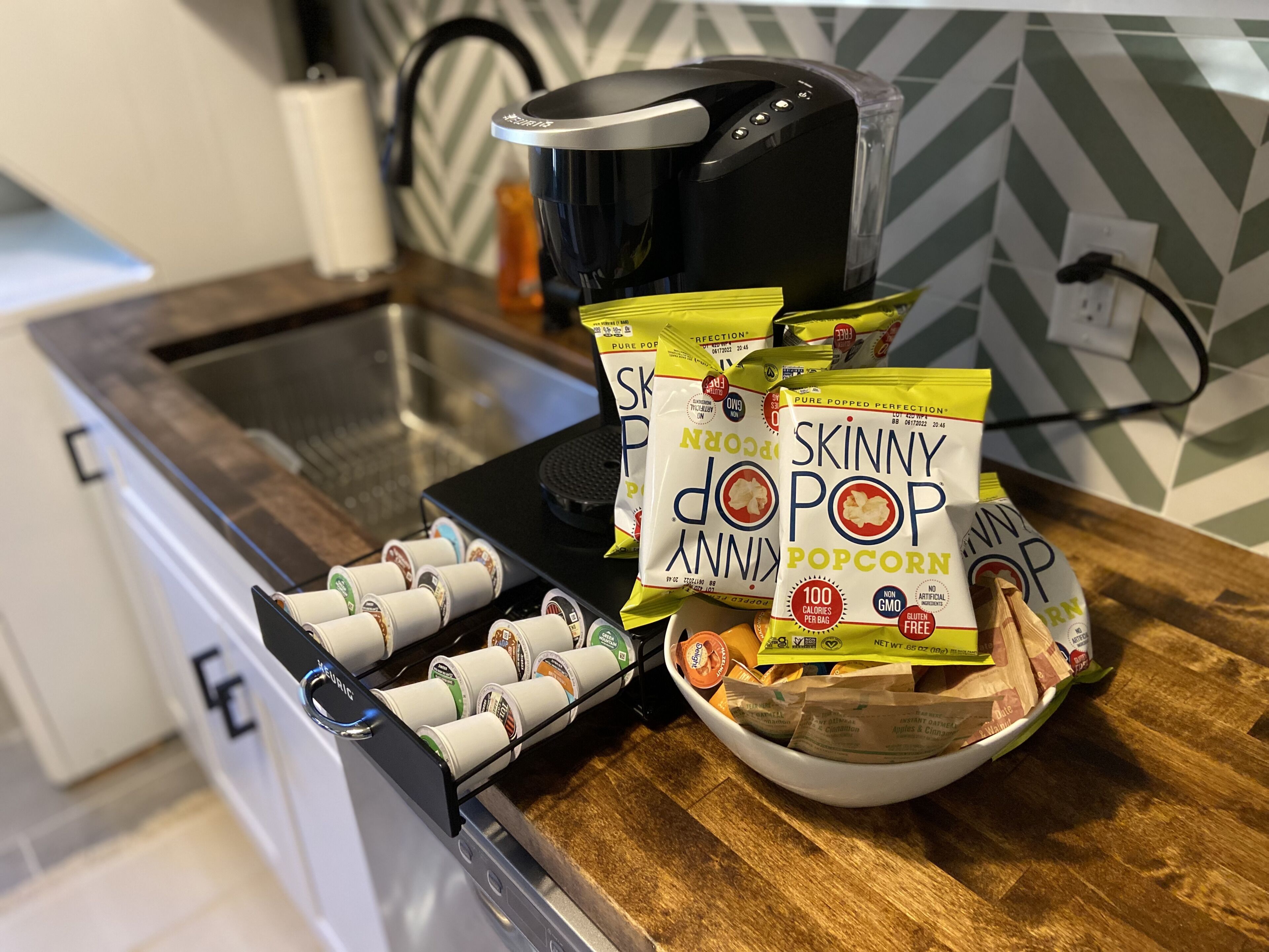 Eine Küchenarbeitsplatte mit einer Kaffeemaschine, einer Schüssel Popcorn und mehreren Packungen Skinny Pop Popcorn.