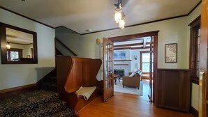 A spacious living room with a wooden floor, a large mirror, a staircase, and a view into another room. - Historic home near lake, parks and BVU! Perfect for summer vacay and reunions! (Storm Lake)