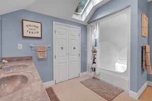 A bathroom with two sinks, a shower, a skylight, and a towel rack.