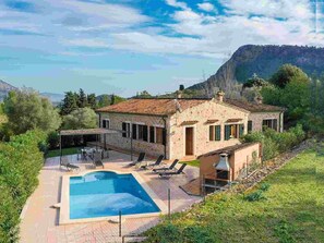 A two-story stone house with a swimming pool, outdoor seating, and a view of the mountains.