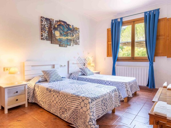 A bedroom with two beds, a nightstand, a lamp, and a window with curtains.