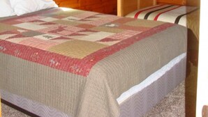 A wooden cabin room with a bunk bed, a quilted bedspread, a window with plaid curtains, and a ceiling light. - On North Twin Lake- Northern Exposure Rentals "Musky Lodge" (Phelps)