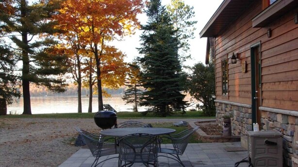A patio with a table and chairs, a grill, and a stone wall. - On North Twin Lake- Northern Exposure Rentals "Musky Lodge" (Phelps)