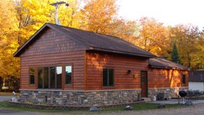 A wooden cabin with a stone foundation, large windows, and a chimney. - On North Twin Lake- Northern Exposure Rentals "Musky Lodge" (Phelps)