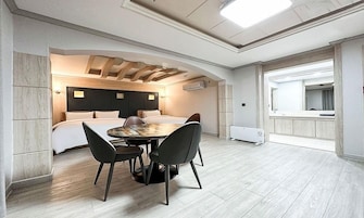 Una habitación de hotel moderna con una cama grande, una zona de comedor con una mesa redonda y sillas, y un baño independiente con espejo y lavabo.
