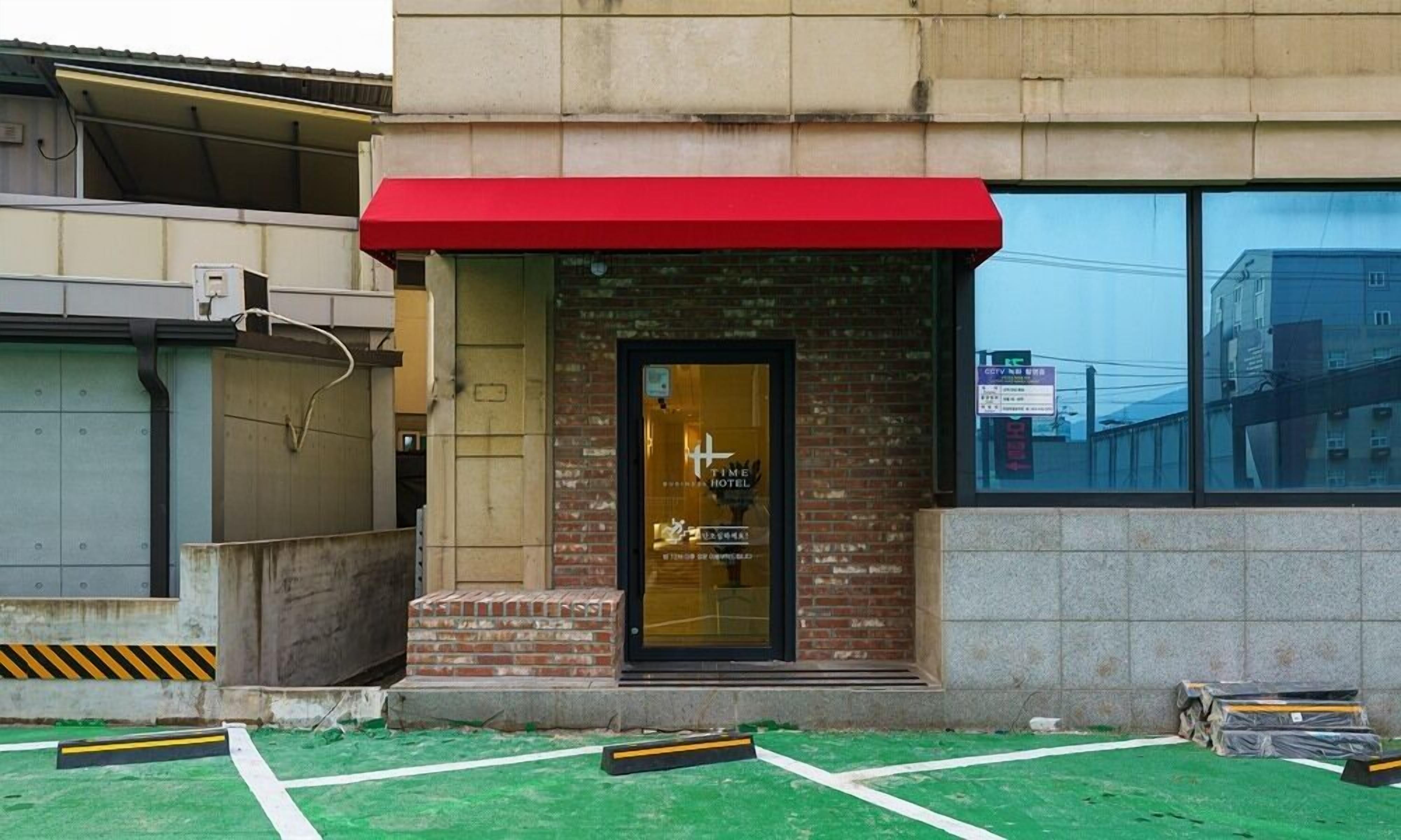A hotel entrance with a red awning, a glass door, and a brick facade.