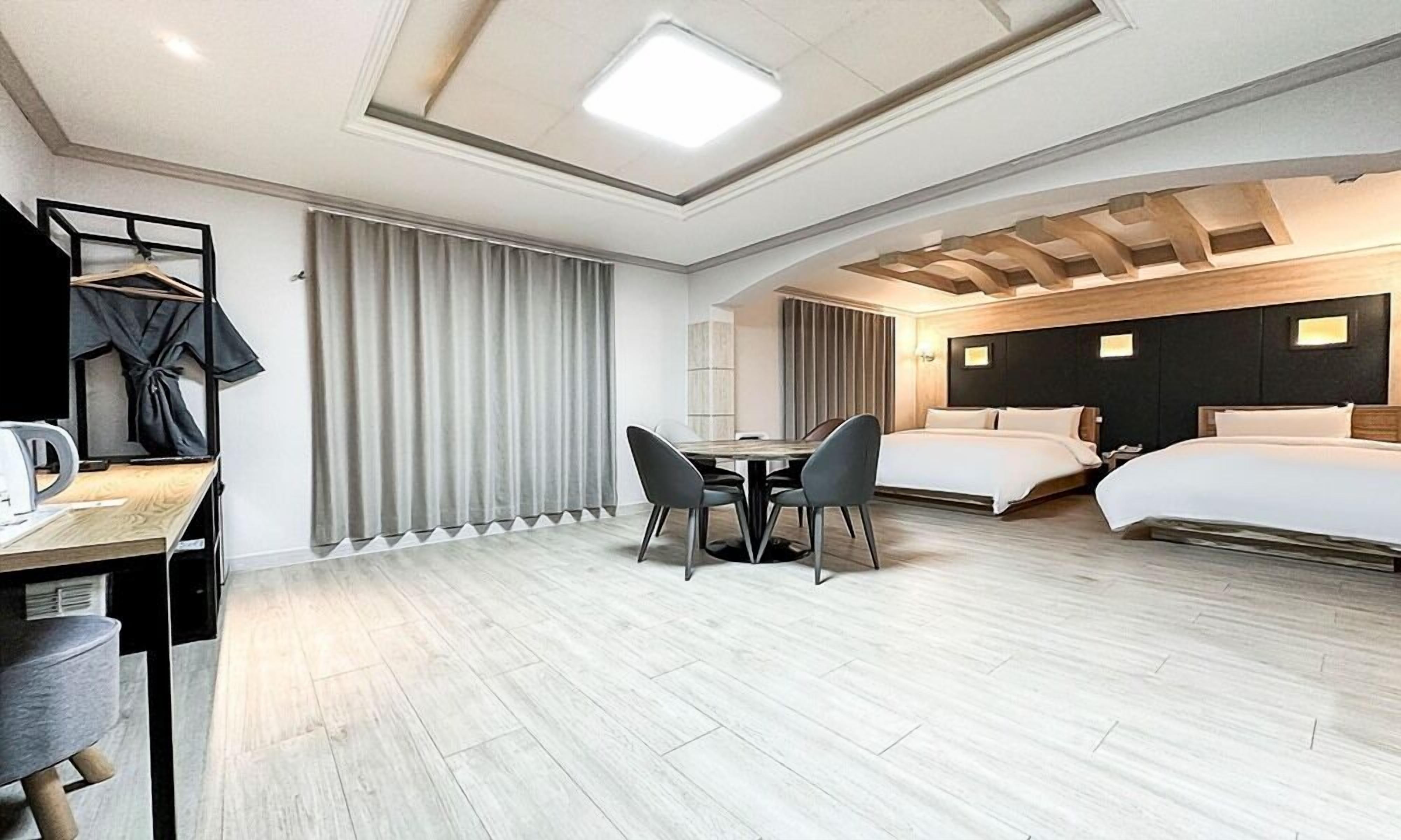 Habitació d'hotel moderna amb dos llits, una taula de dinar amb cadires, un escriptori amb cadira i un armari.
