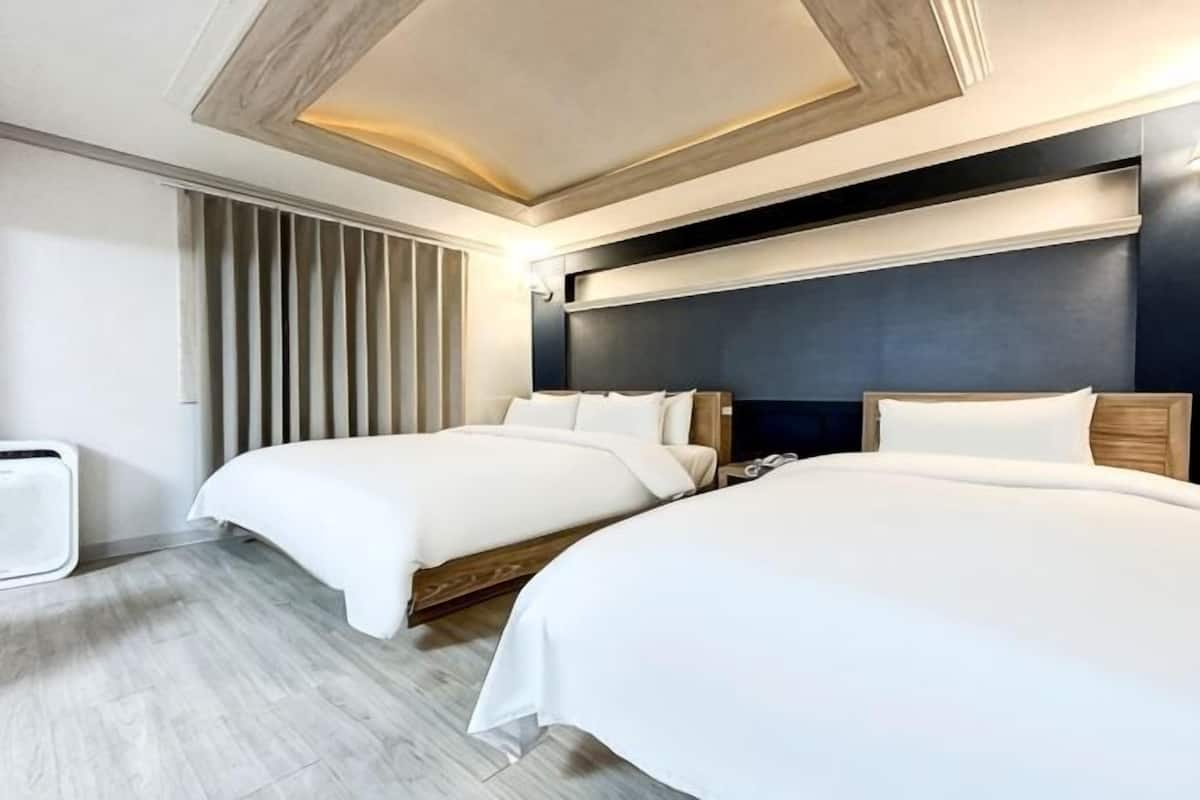 Une chambre d’hôtel avec deux lits, une tête de lit en bois, une lampe fixée au mur et un radiateur.