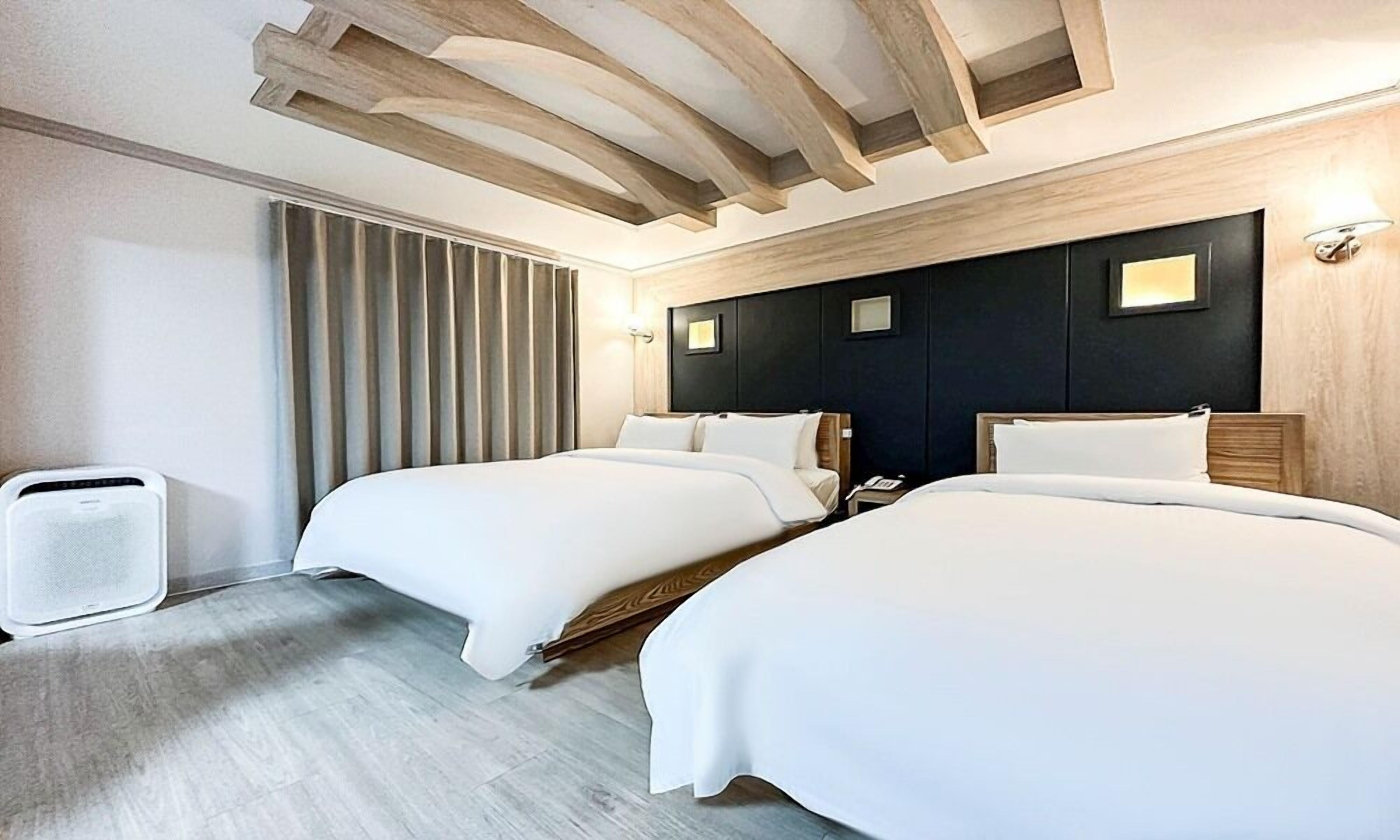 Habitación de hotel con dos camas, techo de madera, un ventanal grande con cortinas y un teléfono instalado en la pared.