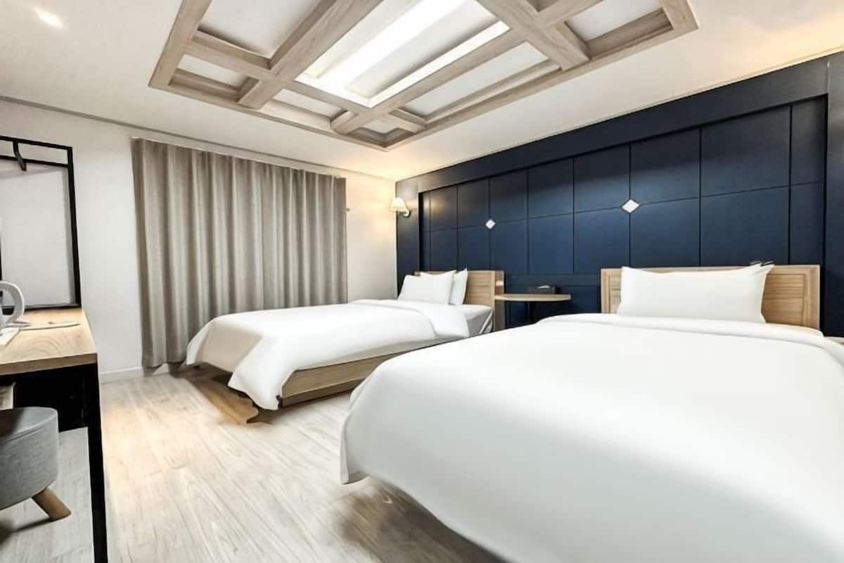 Une chambre d’hôtel avec deux lits, un bureau et une grande fenêtre avec des rideaux.