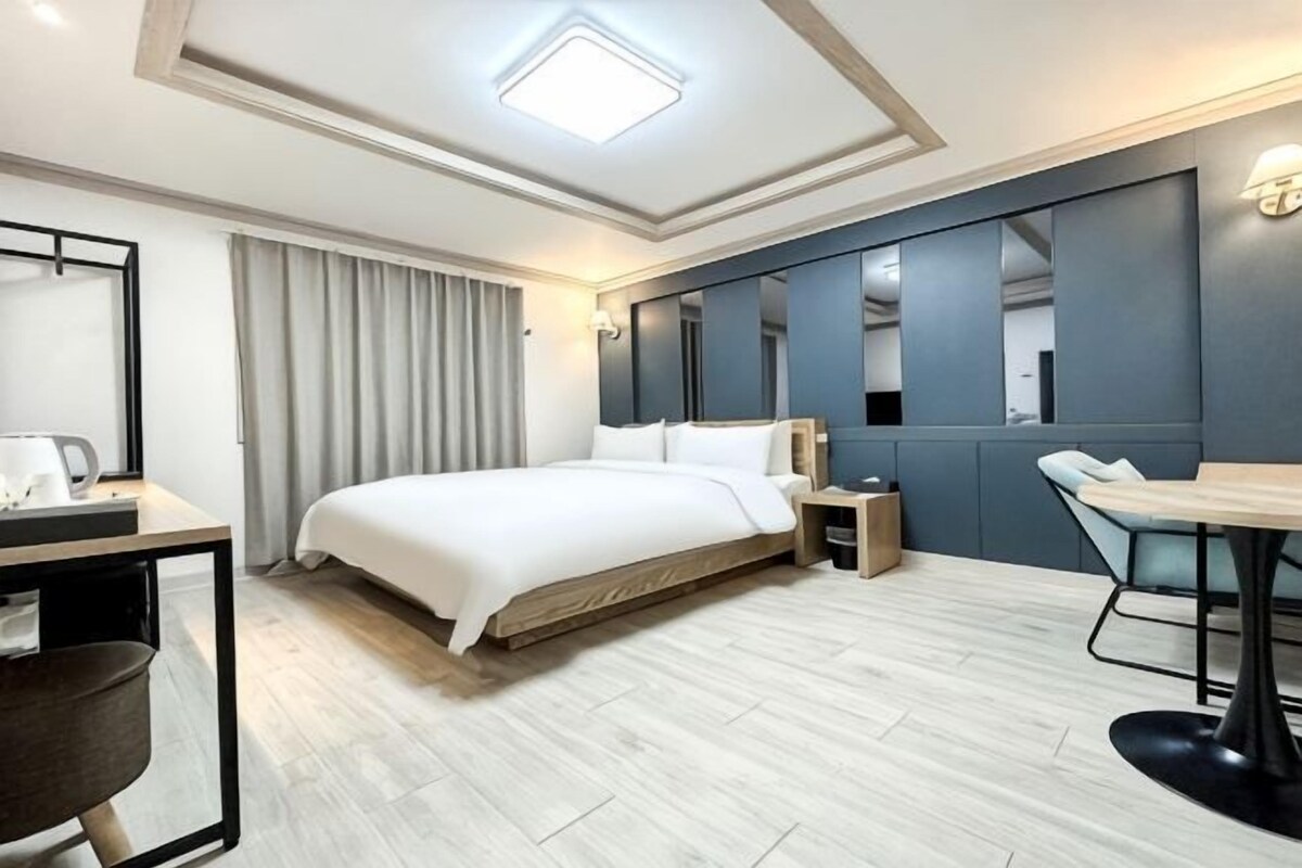 A hotel room with a bed, bedside table, lamp, desk, chair, and a large mirror.