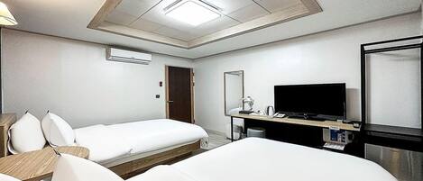 A hotel room with two beds, a desk with a flat-screen TV, a mirror, and an air conditioning unit.