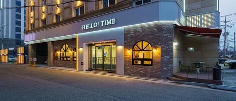 Un hotel con fachada moderna, que presenta un llamativo letrero con la inscripción 'HELLO! TIME' sobre la entrada.