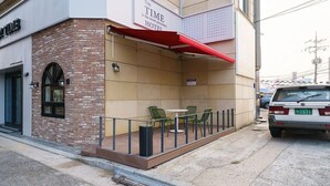 A hotel exterior with a brick facade, a red awning, and outdoor seating with green chairs. - Gumi Time Hotel (Gumi)