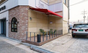 A hotel exterior with a brick facade, a red awning, and outdoor seating with green chairs.
