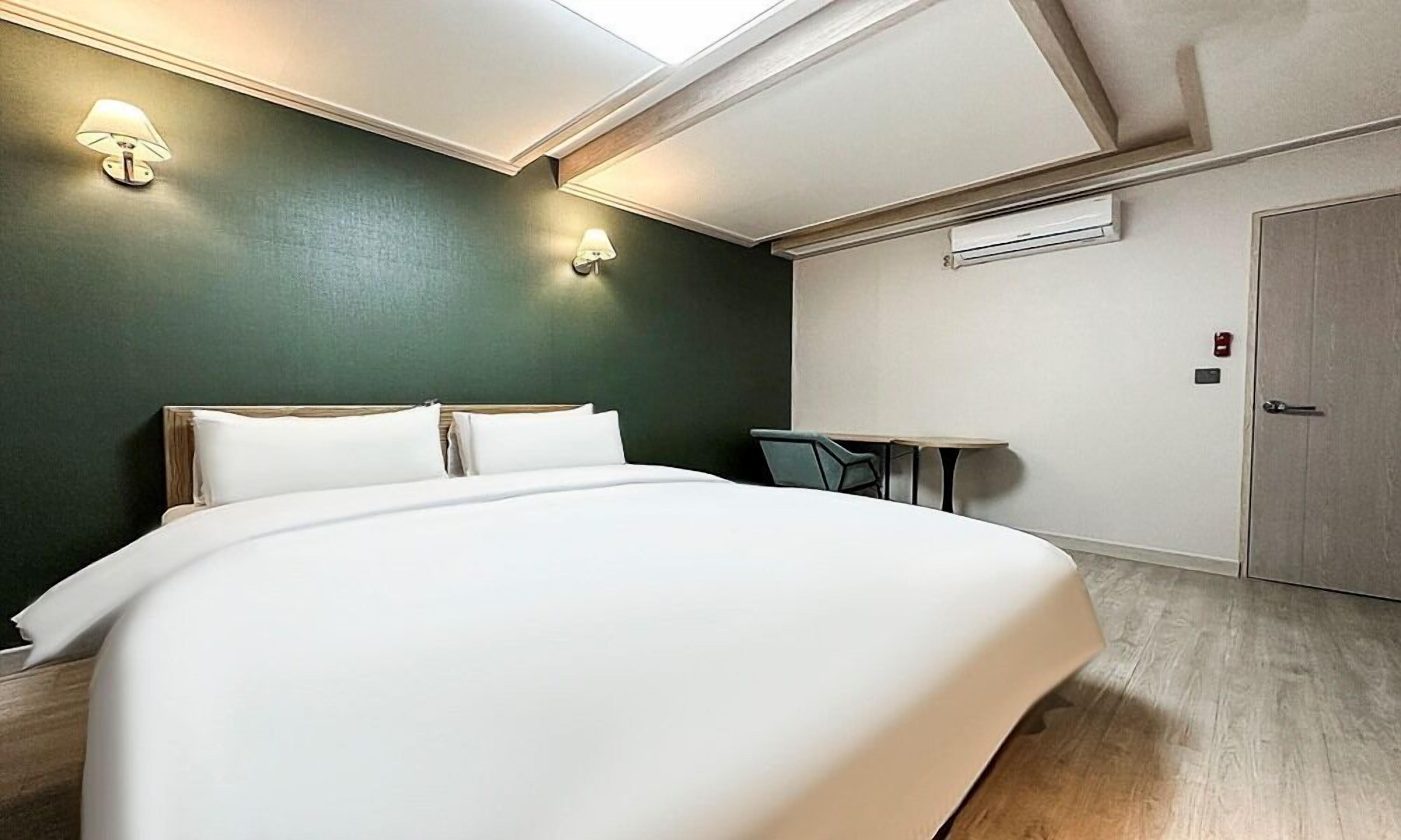 A hotel room with a large bed, a small table, and two wall-mounted lamps.