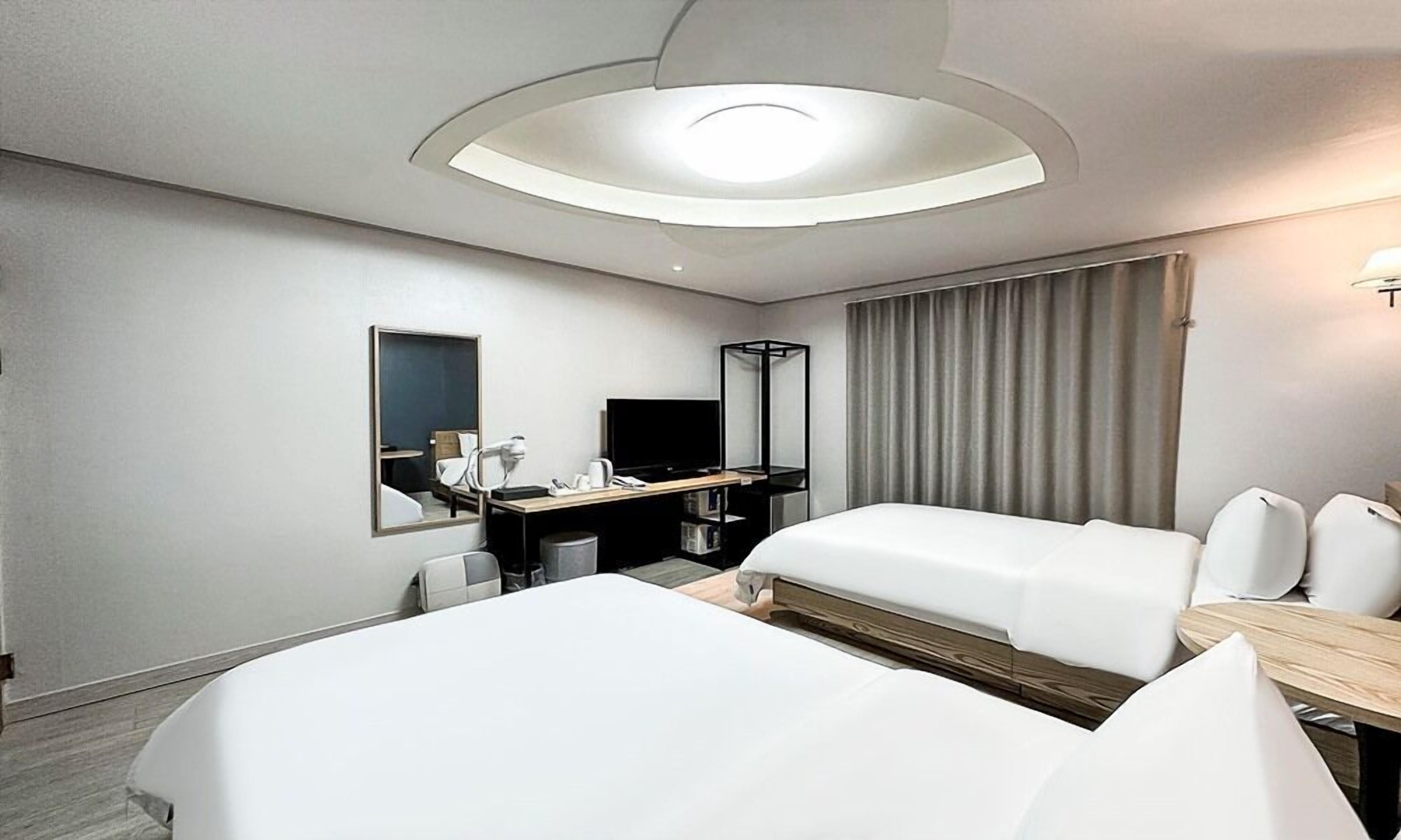 A hotel room with two beds, a desk with a chair, a TV, and a large mirror.