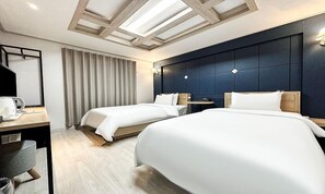 Hotelkamer met twee bedden, een bureau met stoel, een kleine tafel en een groot raam met gordijnen.