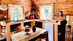 A wooden cabin kitchen with a wooden ceiling, a chandelier, a sink, a refrigerator, and a dining table with chairs. - Wood Cabin in the Smoky Mountains (Sevierville)