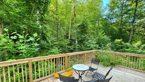 A wooden deck with a round table and four chairs, surrounded by dense greenery. - Wood Cabin in the Smoky Mountains (Sevierville)