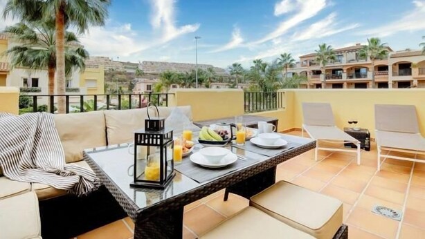 A terrace with a dining table set for breakfast, surrounded by cushioned seating and a view of palm trees and buildings. - 15 Noria Azul Sunny apartment, terrace wifi (La Cala de Mijas)