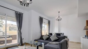 A modern living room with a glass coffee table, grey sofa, and two chandeliers. - 15 Noria Azul Sunny apartment, terrace wifi (La Cala de Mijas)