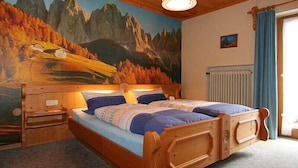 Una cama de madera con cabecera, una mesita de noche y un mural en la pared con un paisaje montañoso.