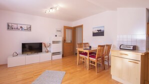 Un espacio habitable compacto con comedor, kitchenette y televisor sobre un mueble blanco.