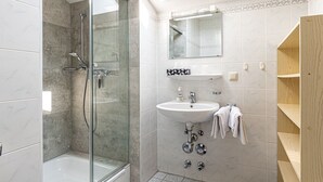 Un baño moderno con tragaluz, cabina de ducha de vidrio, lavamanos y estante de madera.