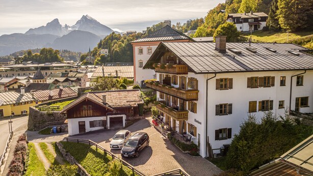 Un edificio de estilo chalé tradicional con tejado inclinado, un balcón con barandilla de madera y vistas al pueblo y montañas circundantes.