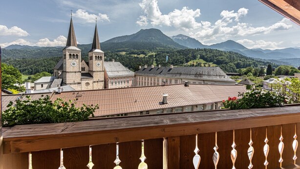 Eine Kirche mit zwei Türmen und ein großes Gebäude mit einem Ziegeldach, vor einer Bergkulisse gelegen.