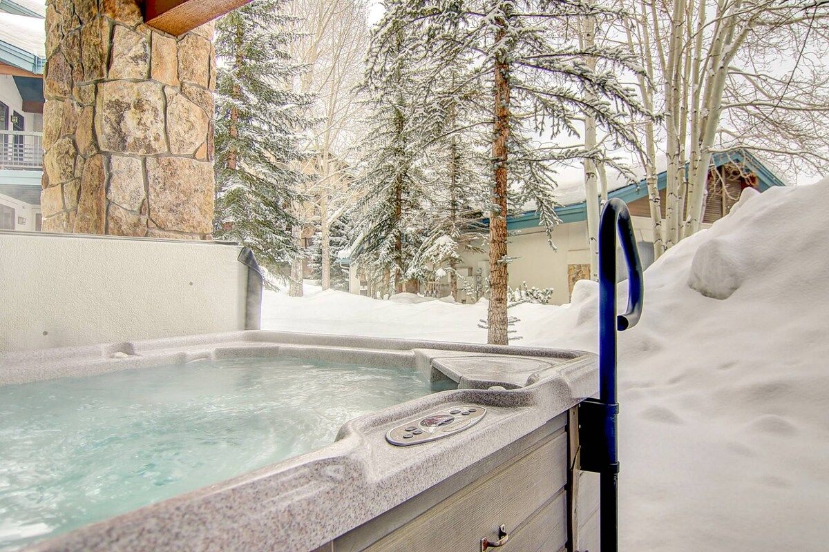 Een hottub met een achtergrond van een stenen muur, omringd door met sneeuw bedekte bomen.