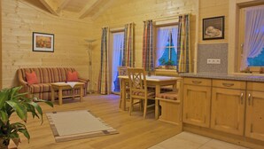 Interior acogedor de una cabaña con una mesa de comedor de madera, sillas, un sofá y una zona de cocina.