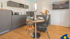 A modern kitchen with grey cabinets, a wooden dining table, and a painting of a boat on the wall.