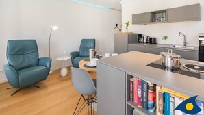 A modern kitchen with a built-in stove, a coffee maker, and a sink. There are two chairs and a small table with a lamp.