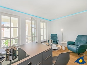 Una cocina moderna con estufa integrada, un comedor con mesa y sillas, y un sillón color turquesa.