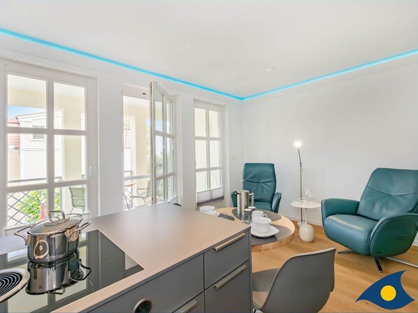 A modern kitchen with a built-in stove, a dining area with a table and chairs, and a teal armchair.