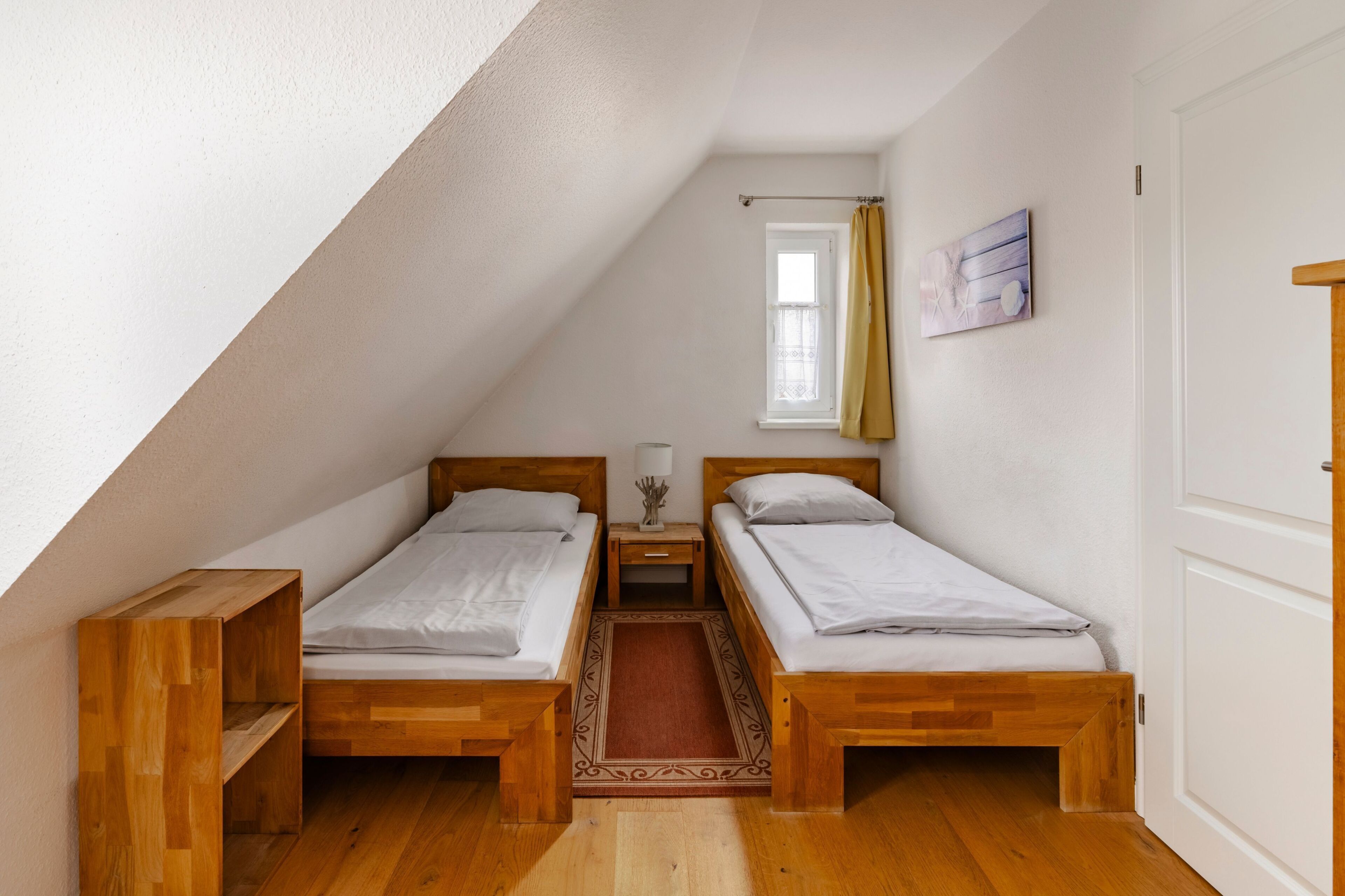 A small, triangular room with two wooden beds, a window with a curtain, and a door.